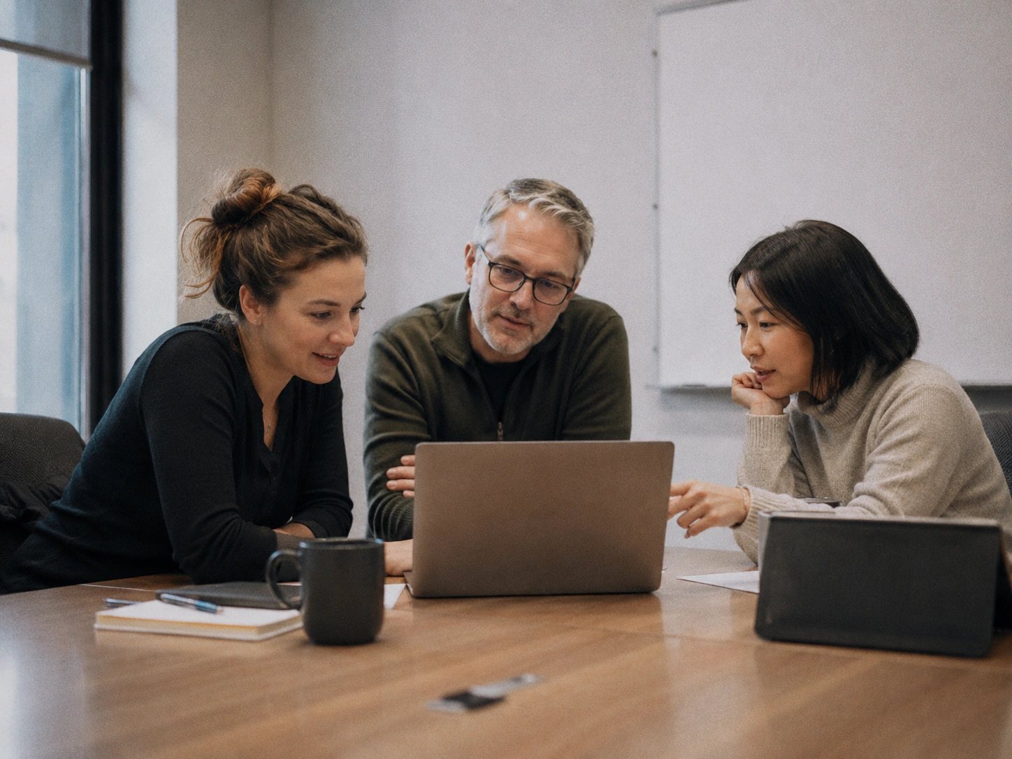 A small group of university staff members collaborating around a laptop in a meeting room, representing the institutional decision-making process for selecting an eBook DRM solution for schools and universities.